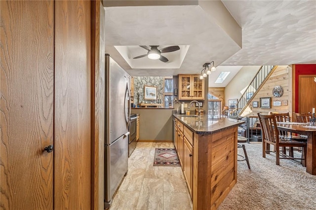 kitchen with glass insert cabinets, brown cabinets, freestanding refrigerator, a peninsula, and a sink