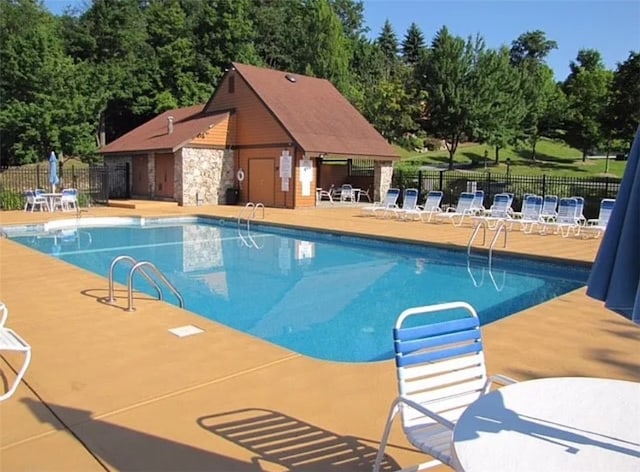 community pool with an outbuilding, a patio area, and fence