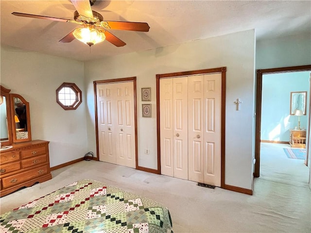 bedroom with a ceiling fan, light carpet, baseboards, and two closets