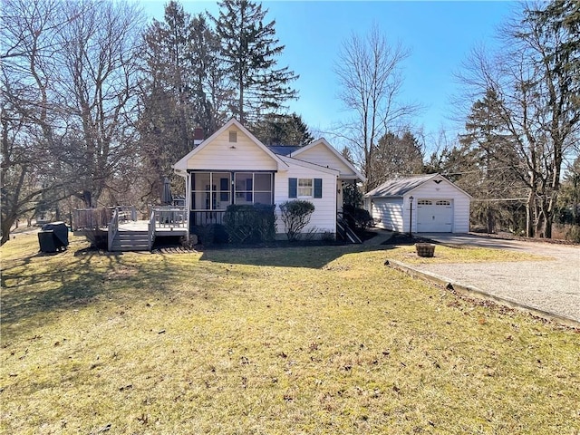 view of front of property featuring a sunroom, a detached garage, an outbuilding, a wooden deck, and a front lawn