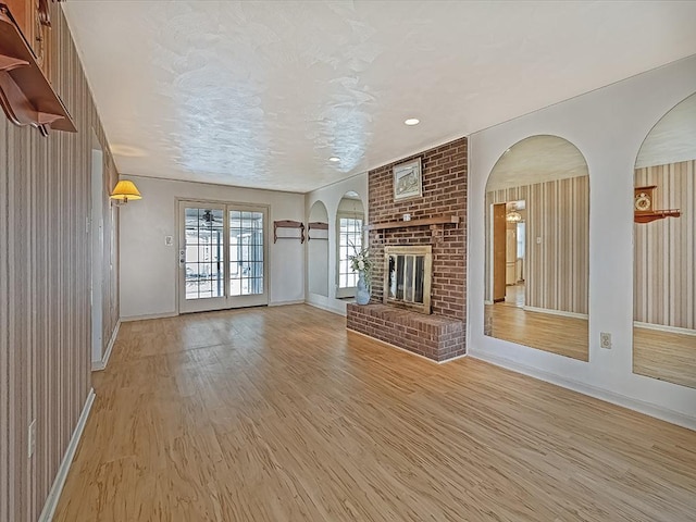 unfurnished living room featuring light wood-style floors, a fireplace, a textured ceiling, and baseboards