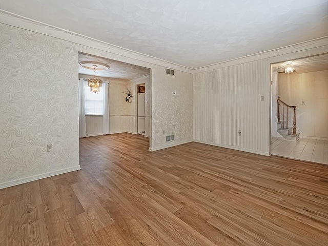 empty room featuring visible vents, stairway, ornamental molding, wood finished floors, and wallpapered walls