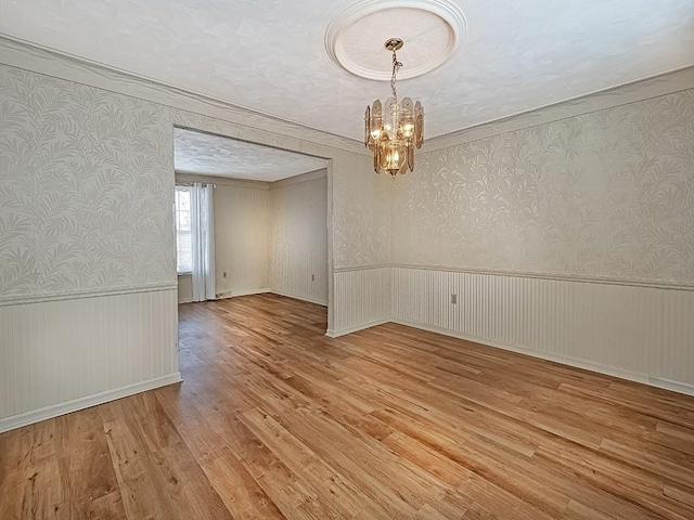 unfurnished room with wainscoting, light wood-style flooring, an inviting chandelier, and wallpapered walls