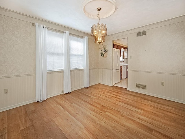 unfurnished room with light wood finished floors, a notable chandelier, wallpapered walls, and wainscoting