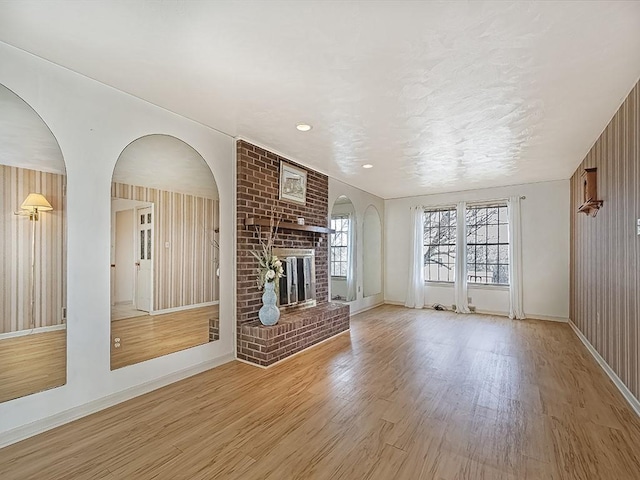 unfurnished living room with light wood finished floors, a brick fireplace, and baseboards