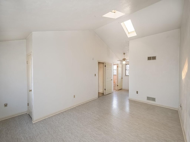 spare room with lofted ceiling with skylight, visible vents, light wood finished floors, and a ceiling fan