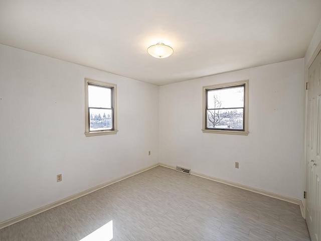 spare room featuring light wood-style flooring, visible vents, and baseboards