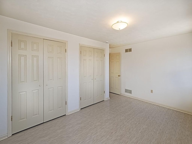 unfurnished bedroom featuring baseboards, light wood-style floors, visible vents, and multiple closets