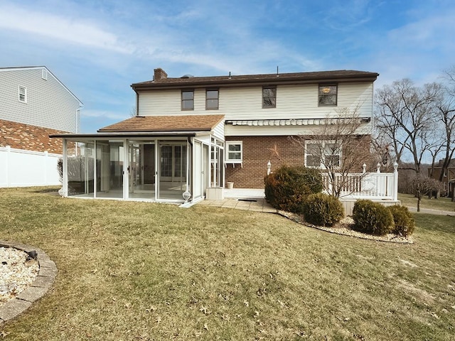 rear view of property featuring brick siding, fence, a sunroom, a yard, and a chimney