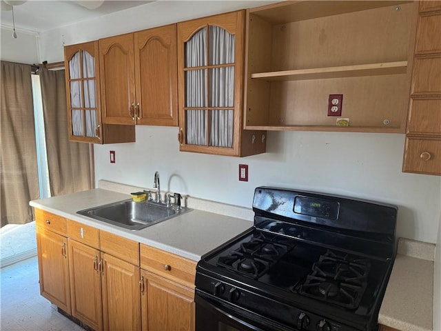 kitchen with brown cabinetry, black range with gas stovetop, light countertops, open shelves, and a sink