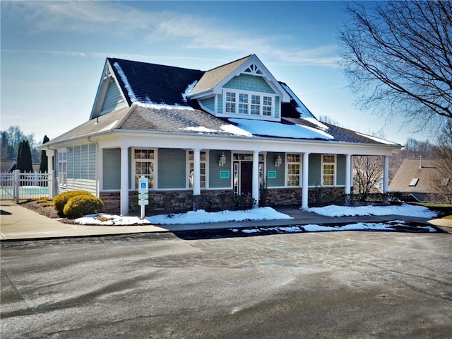 view of front facade with covered porch, stone siding, and fence