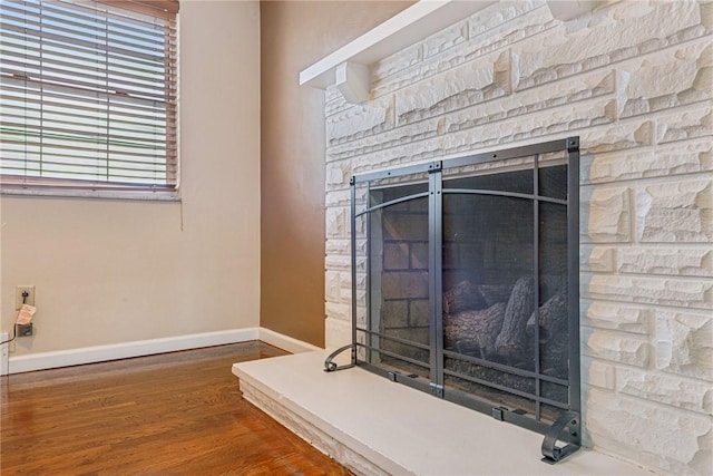 interior details with a stone fireplace, wood finished floors, and baseboards