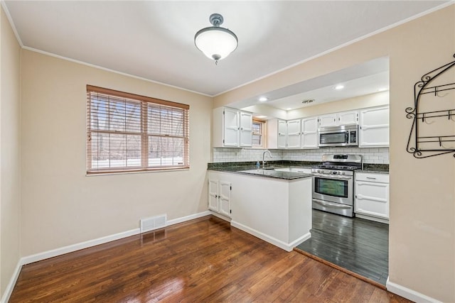 kitchen with appliances with stainless steel finishes, dark countertops, a peninsula, and tasteful backsplash