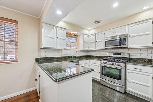 kitchen featuring white cabinets, dark wood-style flooring, a peninsula, stainless steel appliances, and a sink