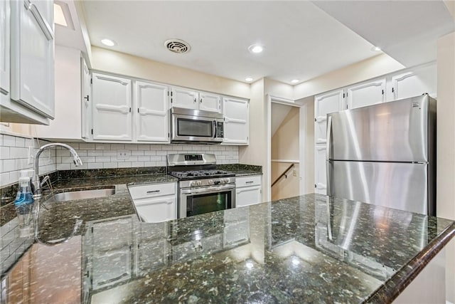 kitchen featuring stainless steel appliances, tasteful backsplash, visible vents, a sink, and dark stone countertops