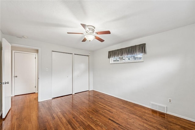 unfurnished bedroom with visible vents, baseboards, ceiling fan, wood finished floors, and two closets