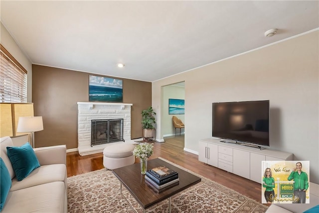 living area featuring crown molding, a stone fireplace, baseboards, and wood finished floors