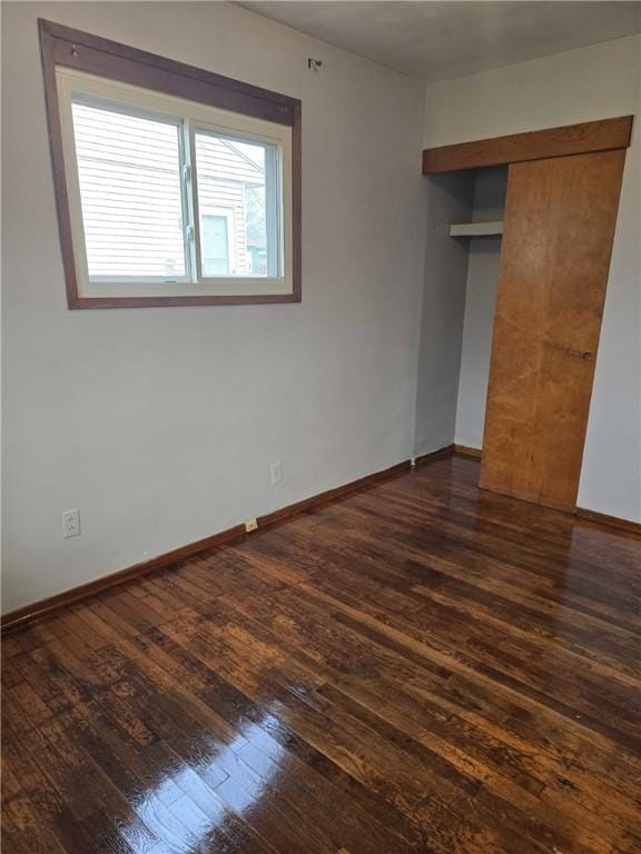 unfurnished bedroom with dark wood-style flooring, a closet, and baseboards