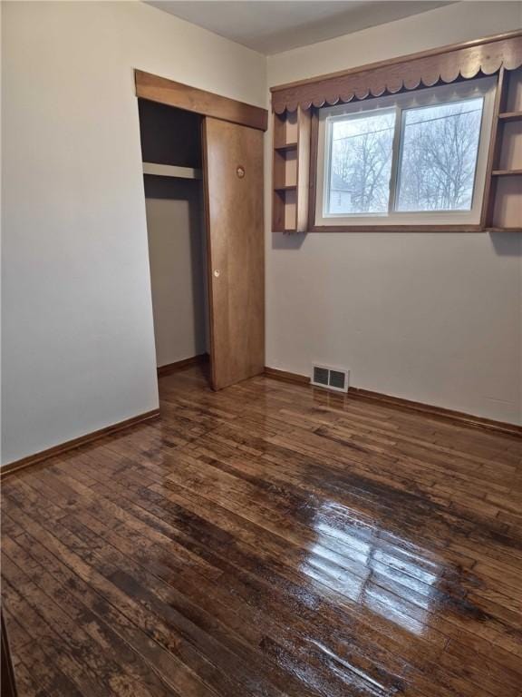 unfurnished bedroom with a closet, visible vents, dark wood finished floors, and baseboards