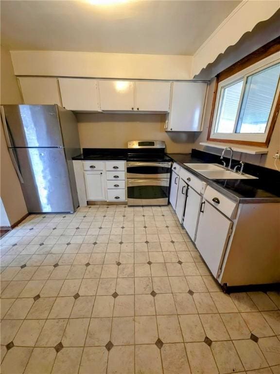 kitchen featuring stainless steel appliances, dark countertops, a sink, and white cabinets