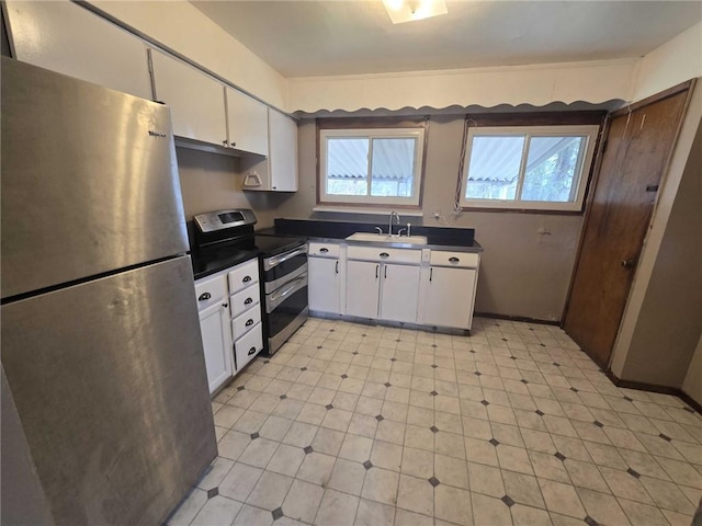 kitchen with light floors, dark countertops, appliances with stainless steel finishes, white cabinets, and a sink