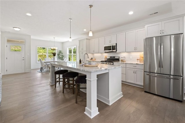 kitchen with dark wood-style flooring, visible vents, appliances with stainless steel finishes, tasteful backsplash, and a center island with sink