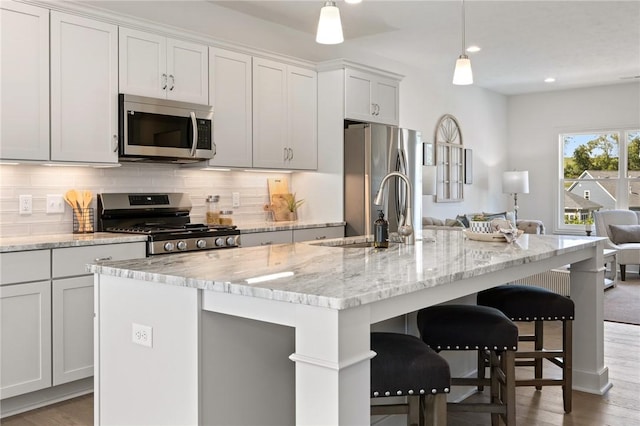 kitchen with a breakfast bar, a center island with sink, stainless steel appliances, tasteful backsplash, and light wood-style flooring