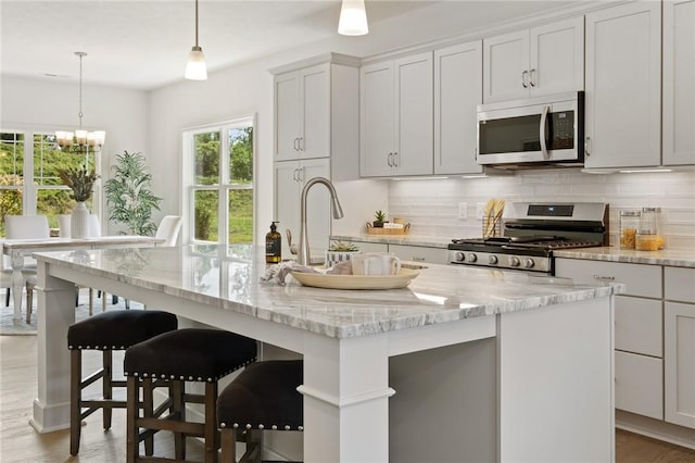 kitchen with appliances with stainless steel finishes, a sink, an island with sink, and tasteful backsplash