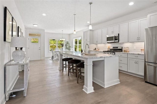 kitchen with light wood finished floors, decorative backsplash, an island with sink, a breakfast bar, and stainless steel appliances