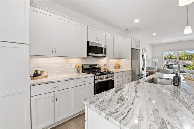 kitchen with pendant lighting, decorative backsplash, appliances with stainless steel finishes, white cabinets, and a sink