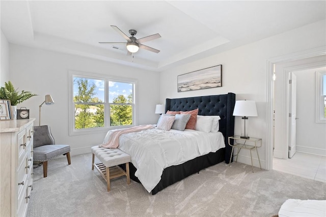 bedroom with baseboards, ceiling fan, a tray ceiling, and light colored carpet