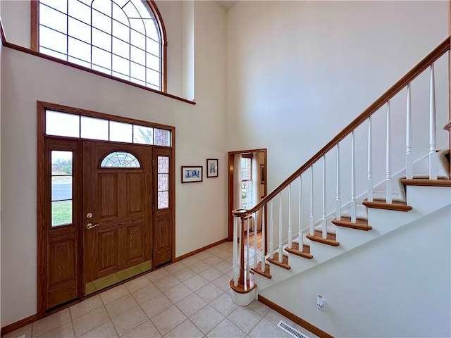 foyer with stairs, light tile patterned floors, a towering ceiling, and baseboards