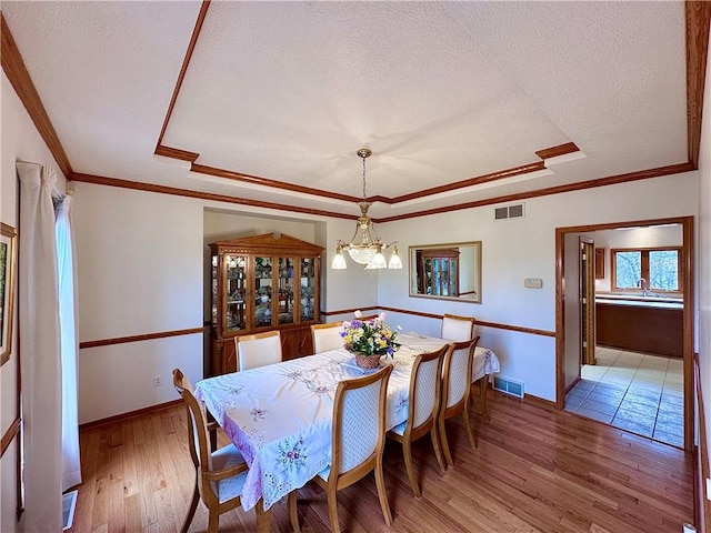 dining room featuring light wood-style flooring, visible vents, a raised ceiling, and a textured ceiling