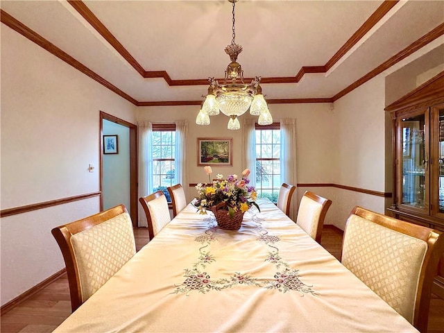 dining area with baseboards, a tray ceiling, wood finished floors, and crown molding