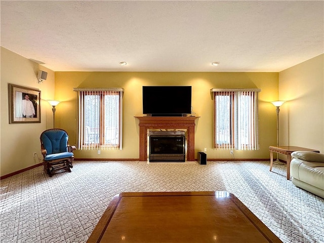 carpeted living room with baseboards, a textured ceiling, and a glass covered fireplace