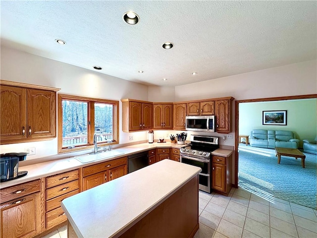 kitchen with a kitchen island, a sink, light countertops, appliances with stainless steel finishes, and brown cabinetry