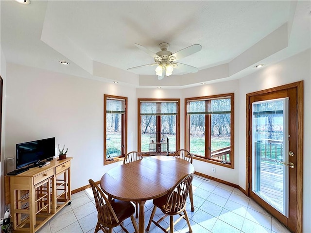 dining space featuring a ceiling fan, a raised ceiling, light tile patterned flooring, and baseboards