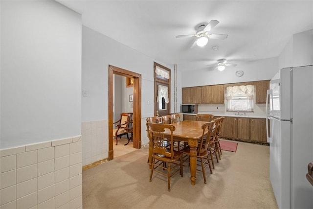 dining room with light carpet, tile walls, and a ceiling fan