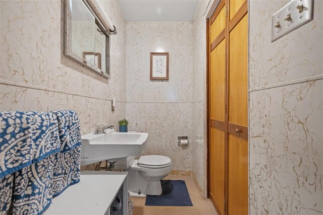 bathroom featuring toilet, tile walls, and a sink