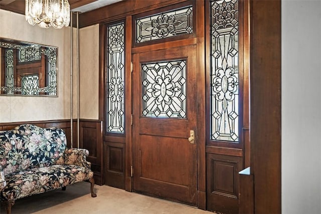 carpeted foyer entrance featuring a notable chandelier and wainscoting