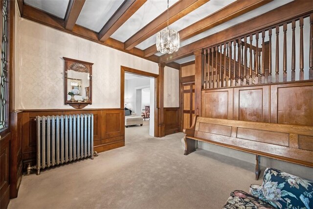 interior space featuring carpet flooring, wainscoting, radiator, beamed ceiling, and an inviting chandelier