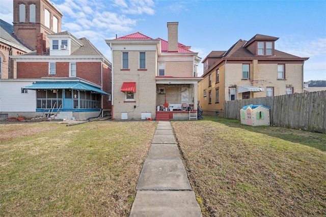 back of house featuring brick siding, a sunroom, fence, and a yard