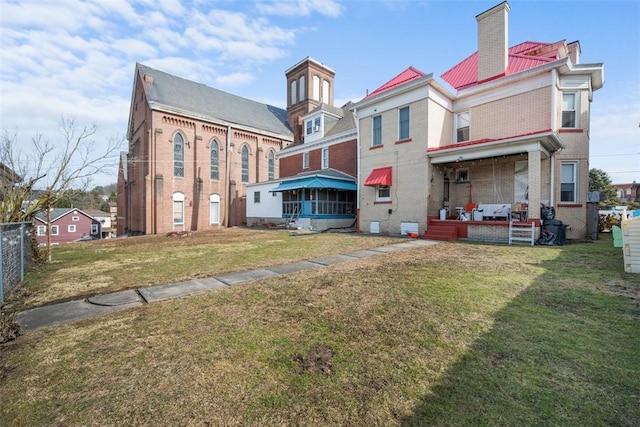 back of property with brick siding, a chimney, fence, and a lawn