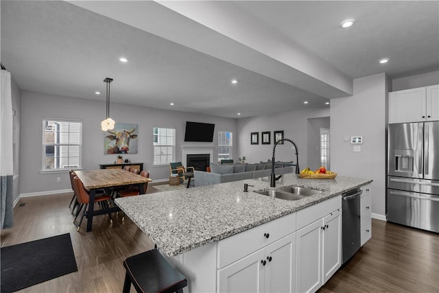 kitchen featuring a kitchen island with sink, a fireplace, a sink, appliances with stainless steel finishes, and dark wood finished floors