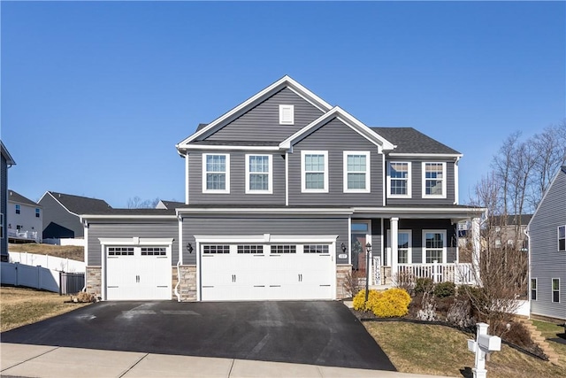 view of front of property with a porch, an attached garage, fence, stone siding, and driveway