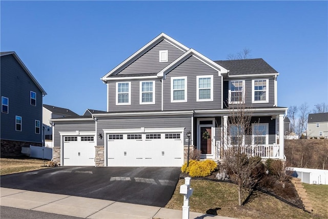 traditional home with aphalt driveway, stone siding, covered porch, and an attached garage