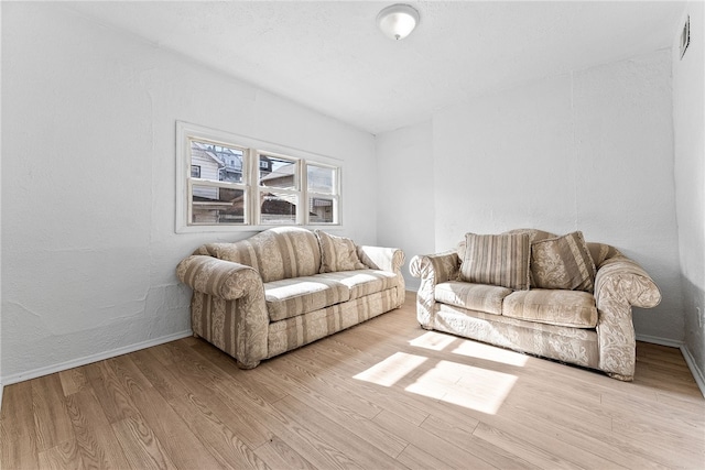 living area with visible vents, a textured wall, light wood-style flooring, and baseboards