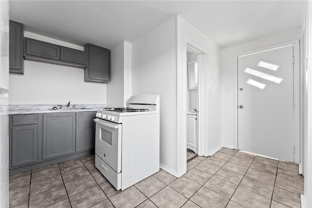 kitchen with light tile patterned floors, white gas range, a sink, and gray cabinetry