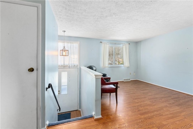 unfurnished room featuring visible vents, a textured ceiling, an upstairs landing, and wood finished floors