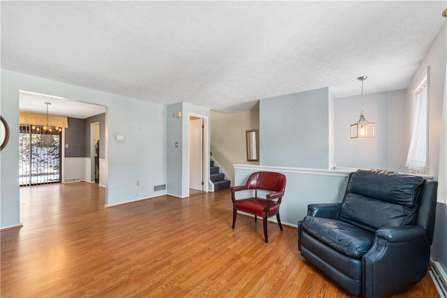 sitting room with light wood finished floors, visible vents, a textured ceiling, a chandelier, and stairs